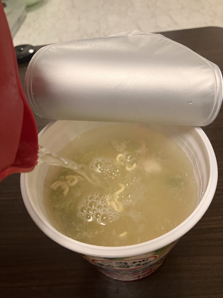 A photo of hot water being poured into the cup noodle